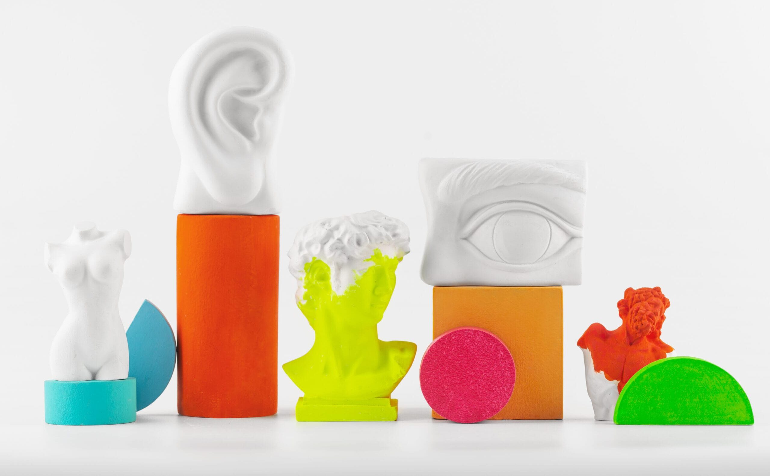 Esculturas y figuras coloridas que simbolizan oído, vista y cuerpo humano en un bodegón minimalista