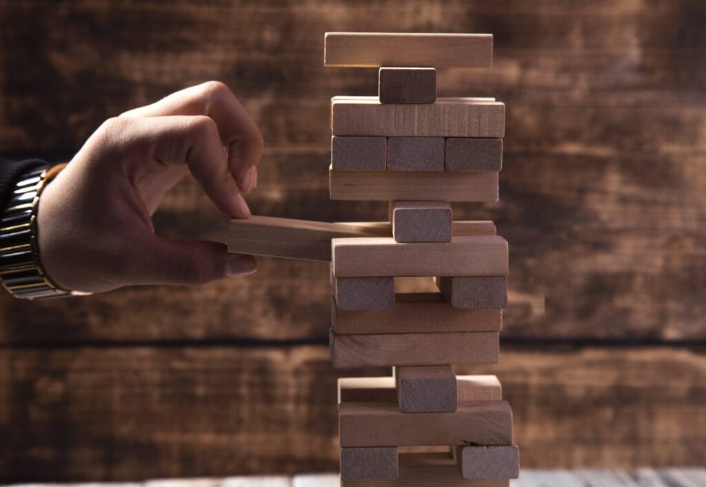 Mano retirando bloque de torre de madera simbolizando riesgo estratégico